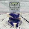 Picture of a box of Shart Wash Natural Handmade Bar Soap Lavender Lemongrass scent sitting on 3 purple and white bars of soap with a wood background