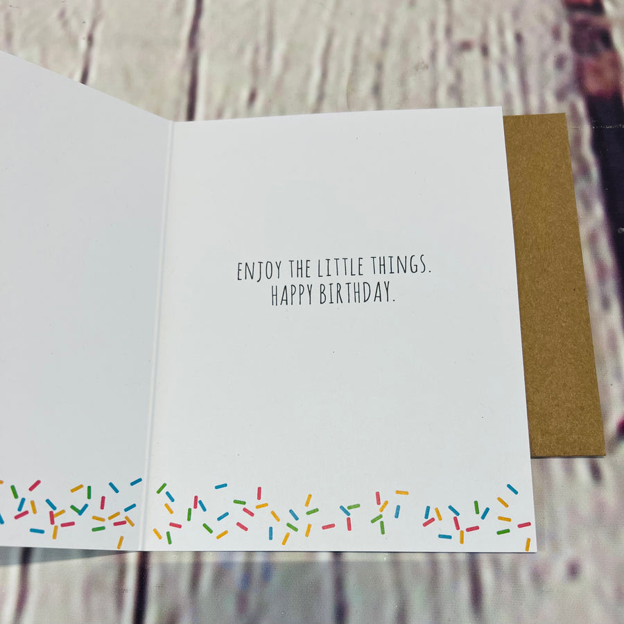Inside of the card. White with sprinkles on the bottom. Text says enjoy the little things. Happy birthday.