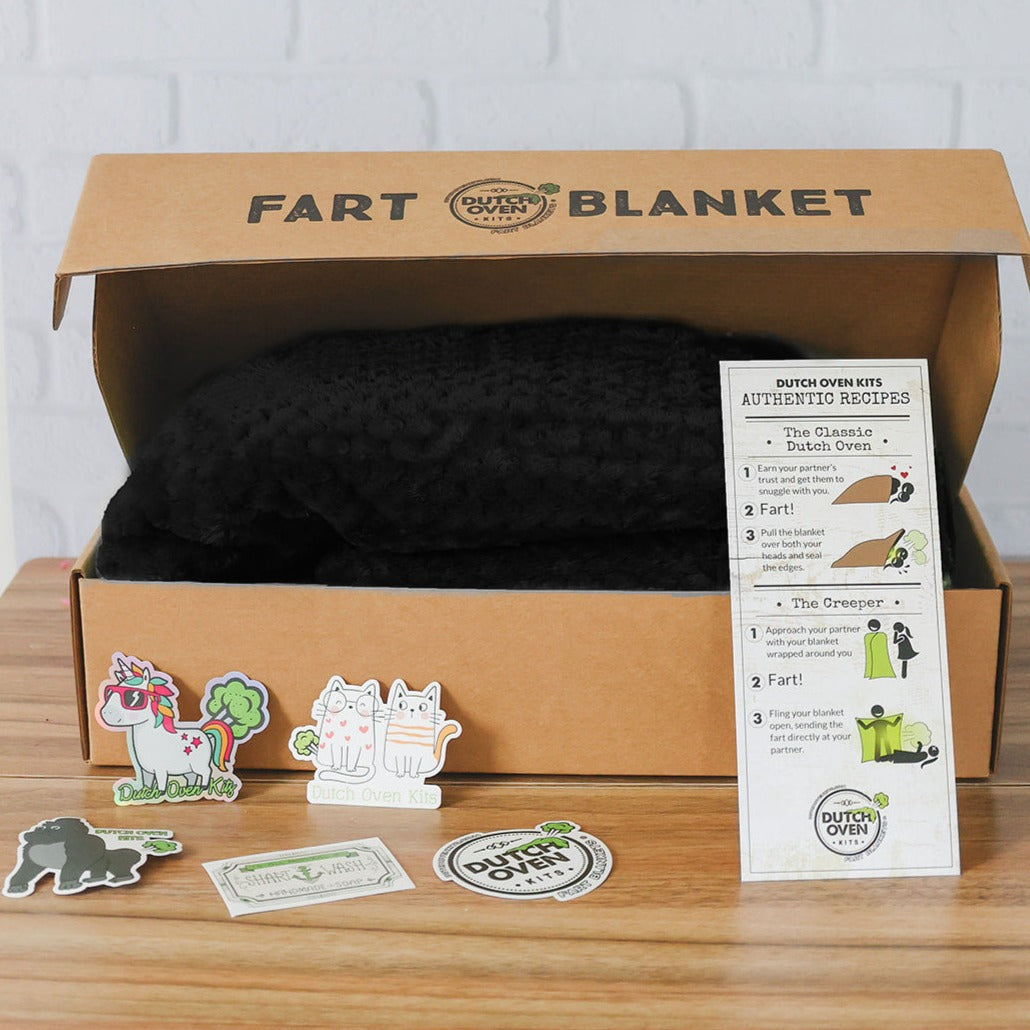 A black dutch oven kits blanket in a box with a recipe card and stickers on a wood background