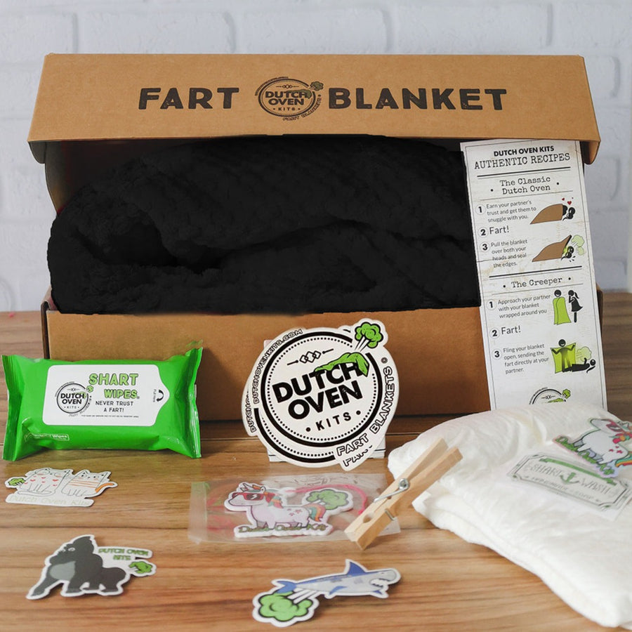 A black blanket inside a box with an adult diaper pack of shart wipes, air freshener, clothes pin and stickers.