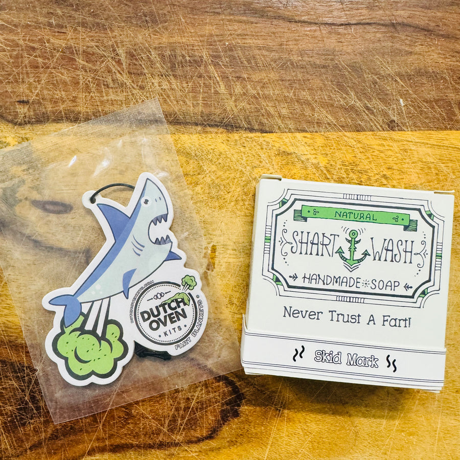 A farting shark air freshener and a bar of Skid Mark shart wash soap on a wooden surface