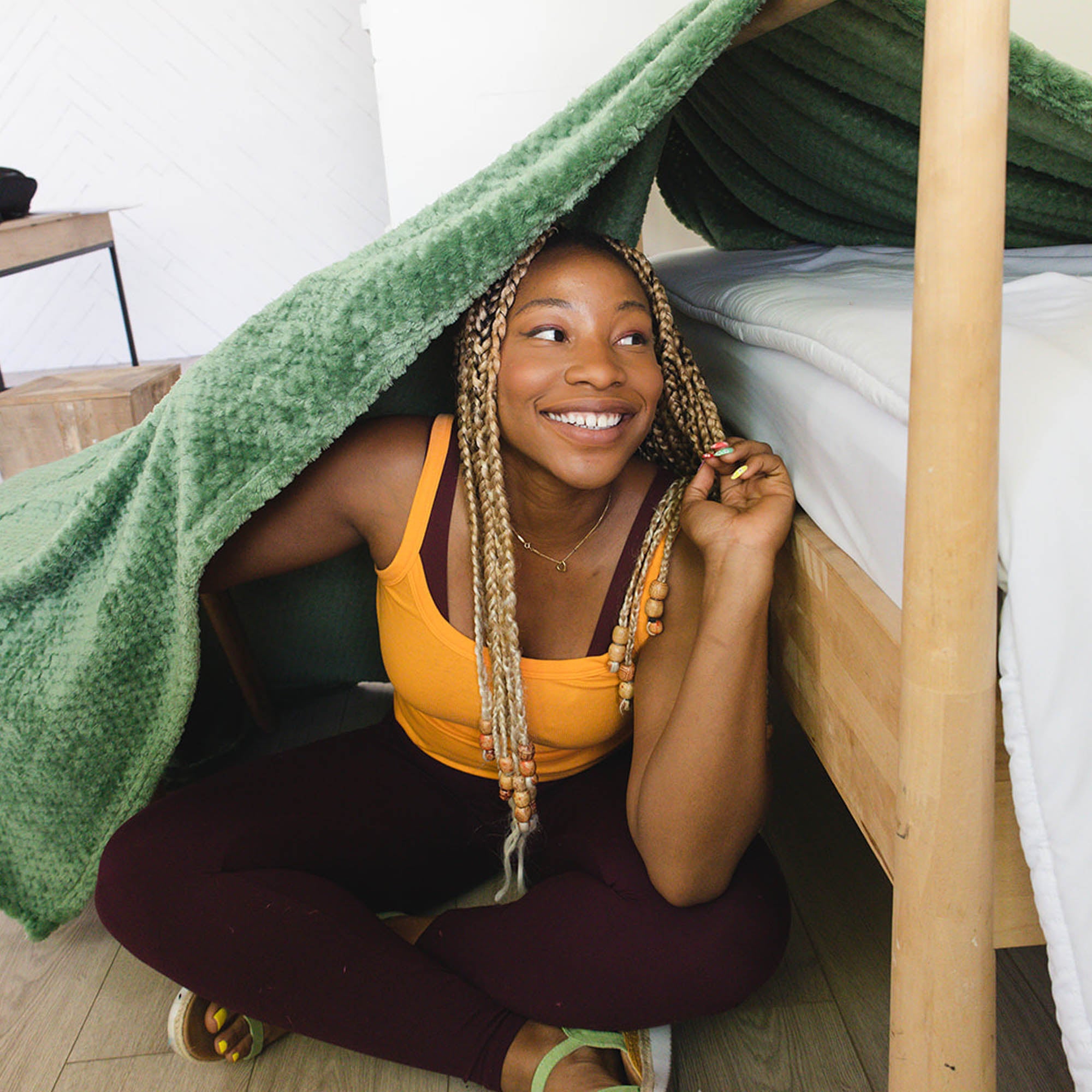 A woman sits inside a blanket fort made with a green blanket