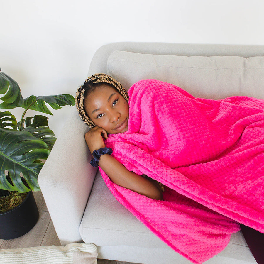 a woman lays on a couch covered by a pink blanket