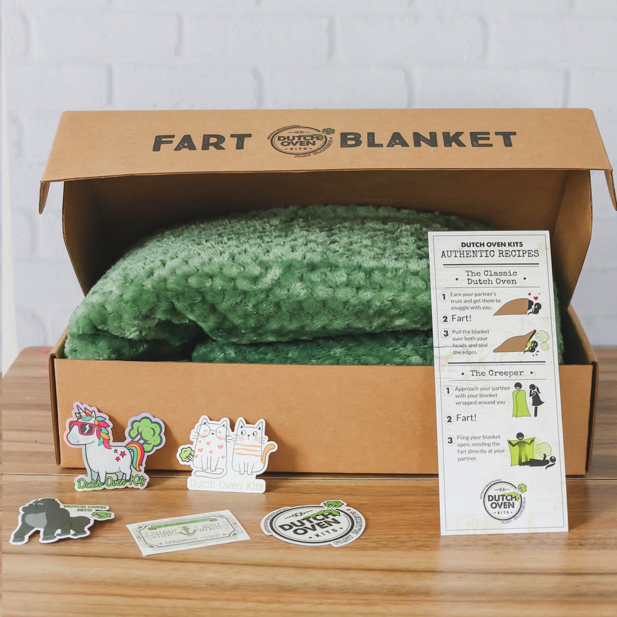 Picture of a fleece throw blanket from Dutch Oven Kits Tactical Green Color close up on  wood floor with a white brick background