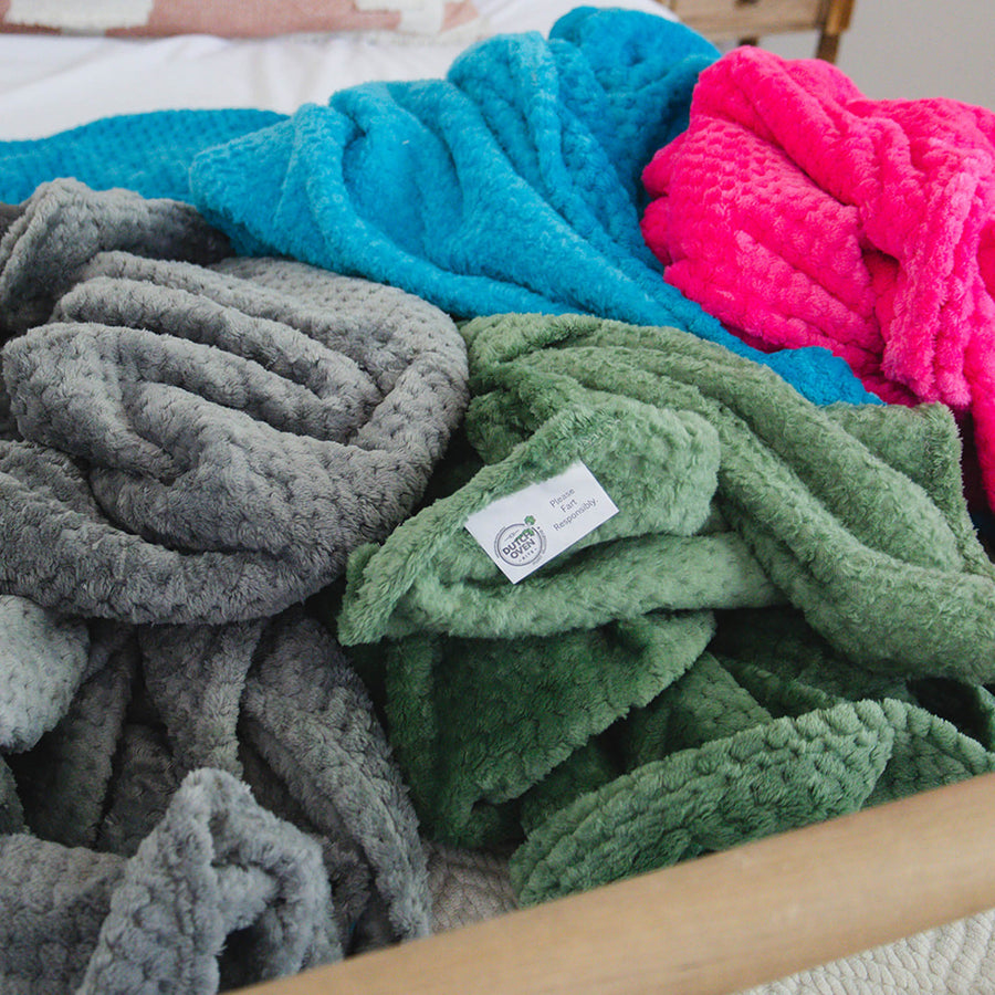 Picture of 4 blankets on a bed. A gray, blue, green and pink.