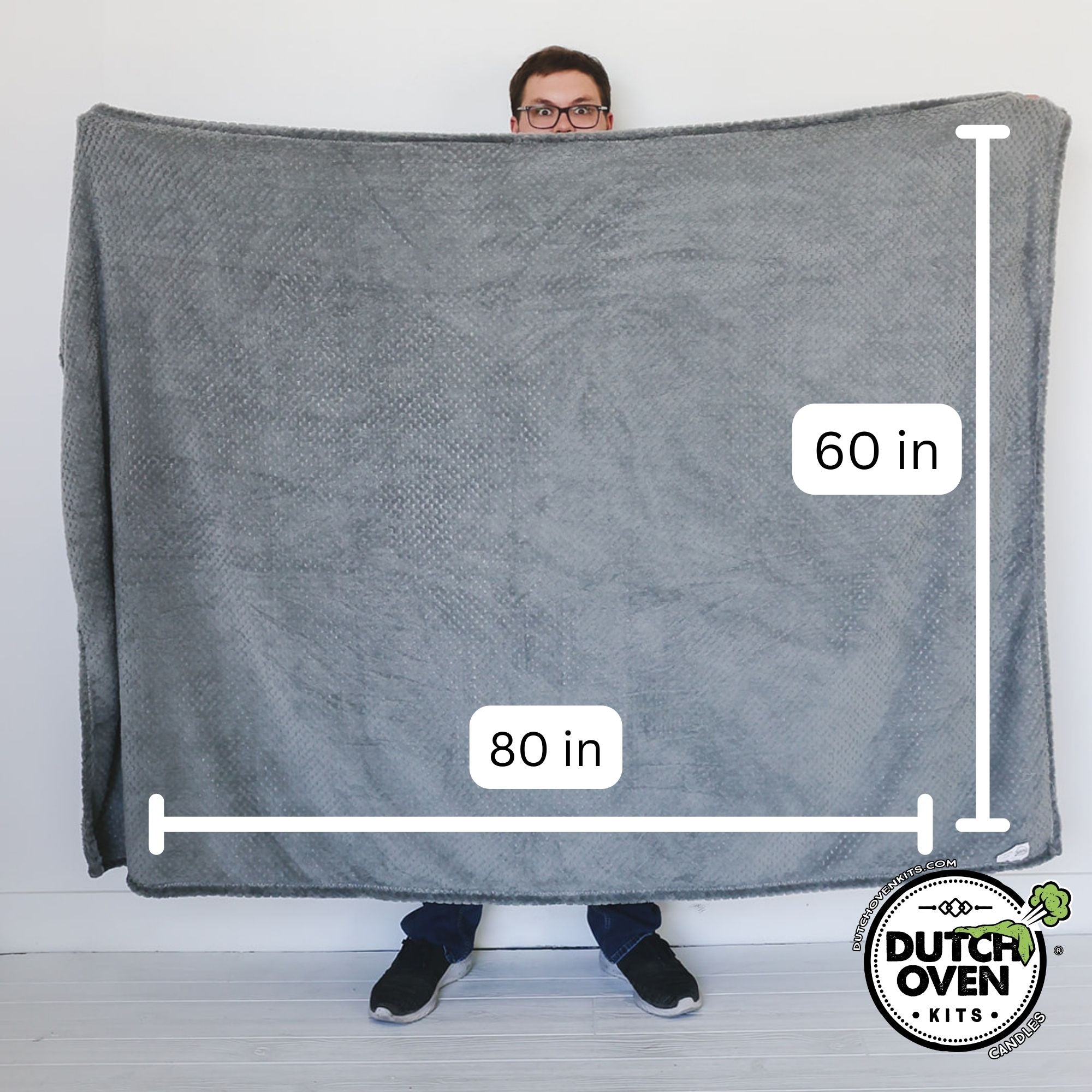 A man holding a blanket showing its size. 60in x 80in