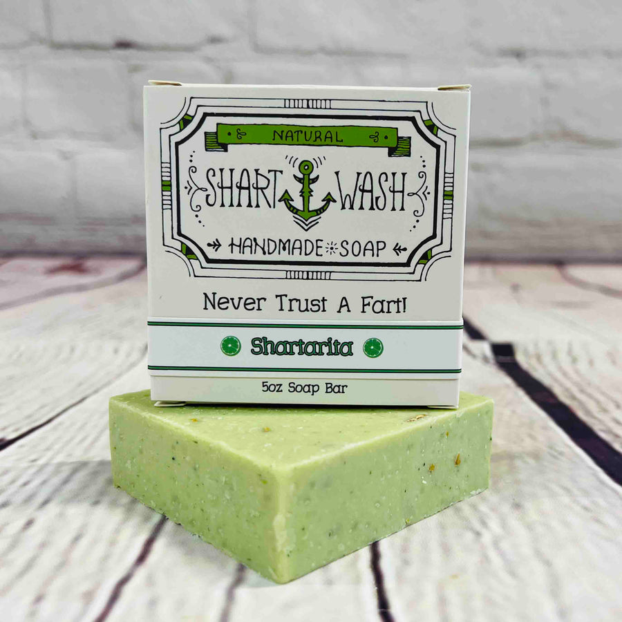 Picture of a box of Shart Wash Natural Handmade Bar Soap Shartarita scent sitting on a green bar of soap with a wood background