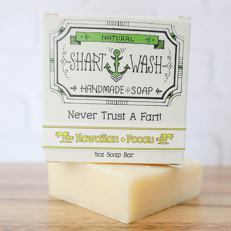Picture of a box of Shart Wash Natural Handmade Bar Soap Hawaiian Pooau scent sitting on a light yellow bar of soap with a wood background