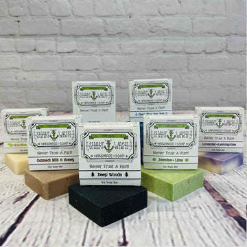 Picture of 7 bars of soap various scents with an exfoliating soap bag on a wood background