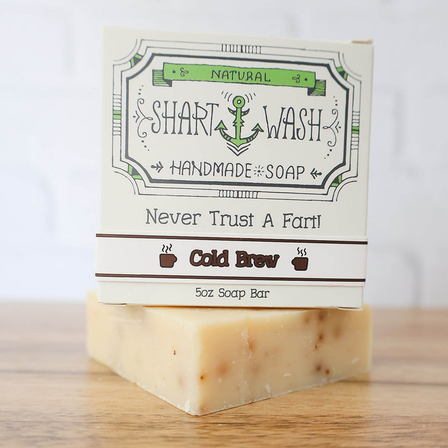 Picture of a box of Shart Wash Natural Handmade Bar Soap Cold Brew Coffee scent sitting on a tan bar of soap with a wood background