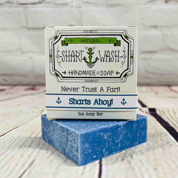 Picture of a box of Shart Wash Natural Handmade Bar Soap Sharts Ahoy scent sitting on a blue bar of soap with a wood background