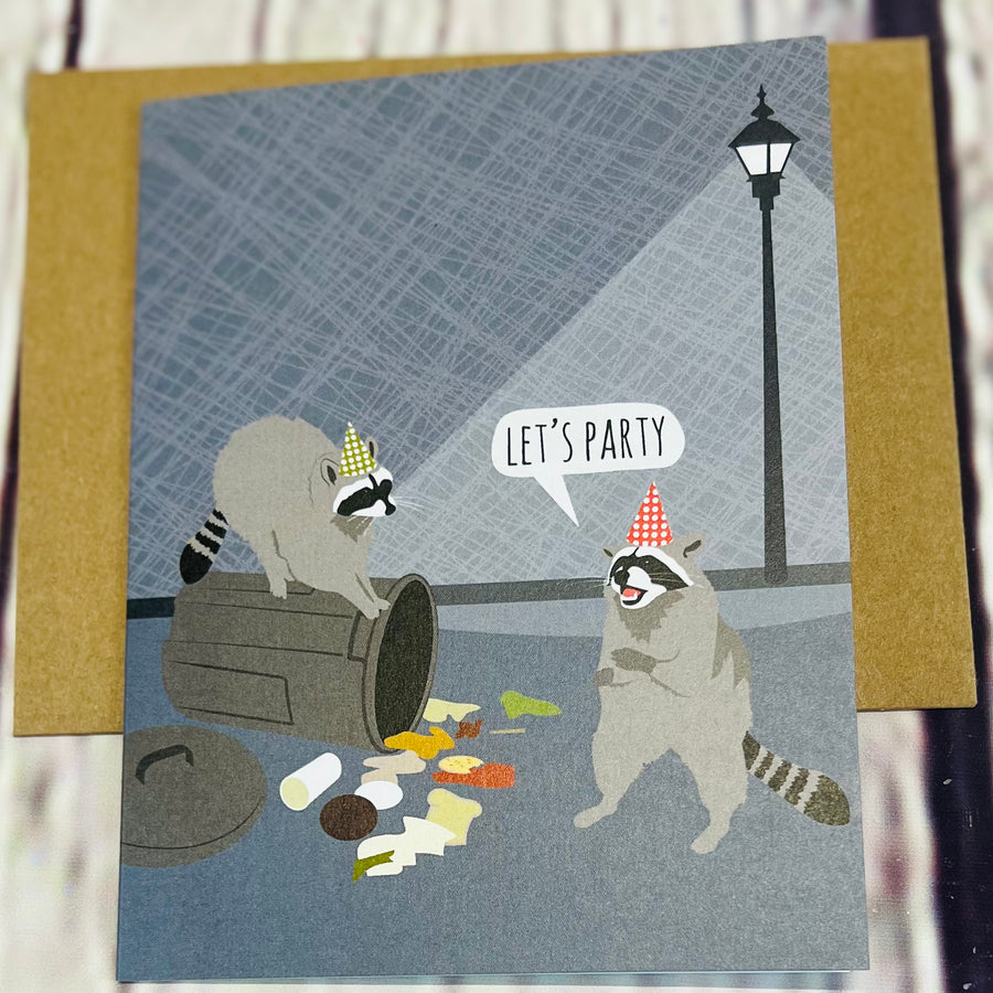 Picture of two raccoons digging in the trash. One is wearing a party hat saying, 