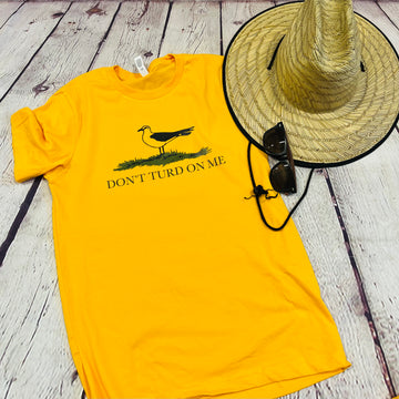 Picture of a gold and yellow t shirt with a picture of a seagull standing in the grass. Text on the shirt says 